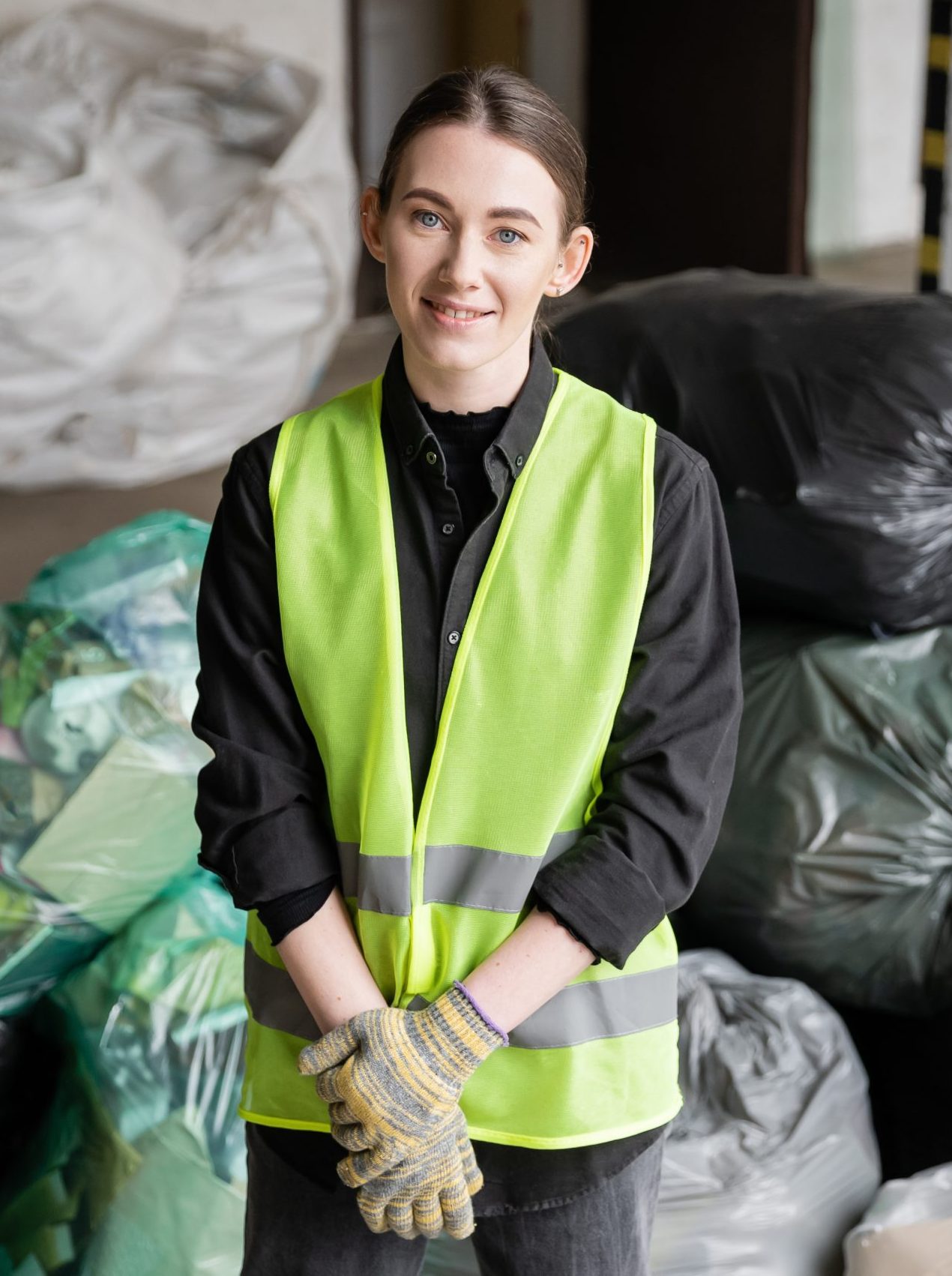 Positive young sorter in reflective vest and protective gloves looking at camera while standing near